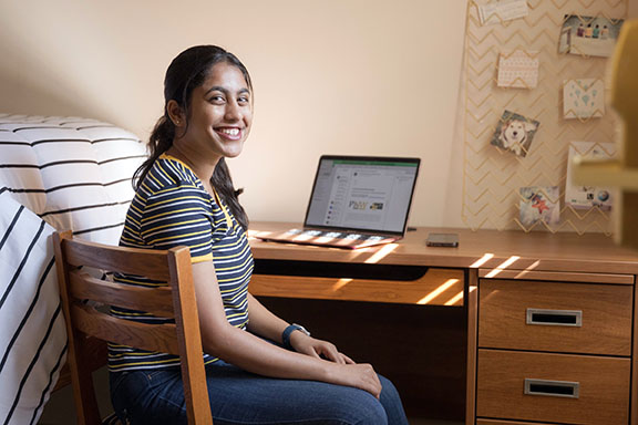 A PNW student sits at a desk in her dorm room.