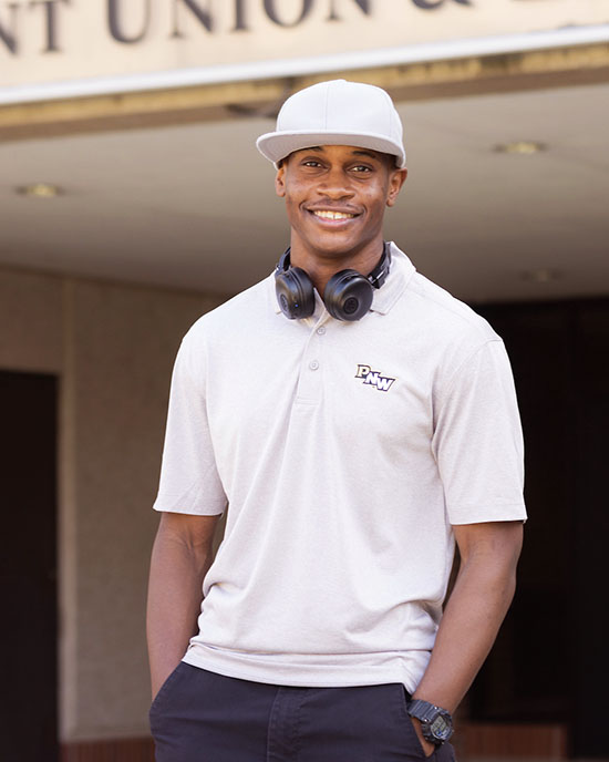 A PNW student stands outdoors in a hat and headphones.