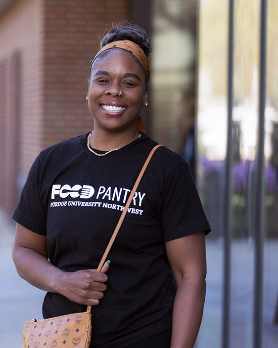 A PNW student in a food pantry shirt stands outdoors