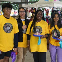 Four students pose together. They are all wearing yellow shirts with the 2024 Hispanic Heritage Month logos on them