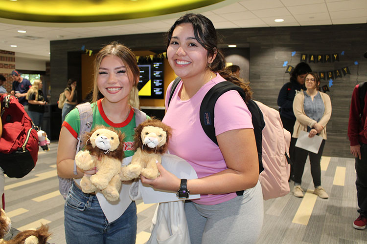 Two students stand in the Mane Zone and hold up lion stuffed animals.