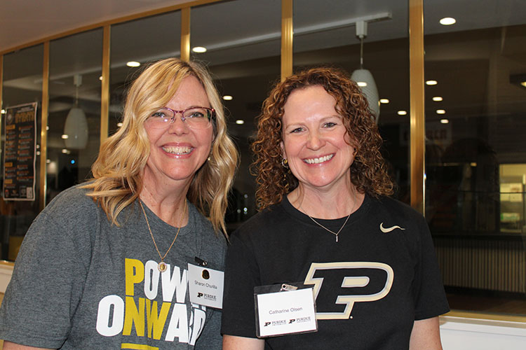 Two people pose together. The person on the right is wearing a black Purdue t-shirt, the person on the left is wearing a gray Power Onward shirt