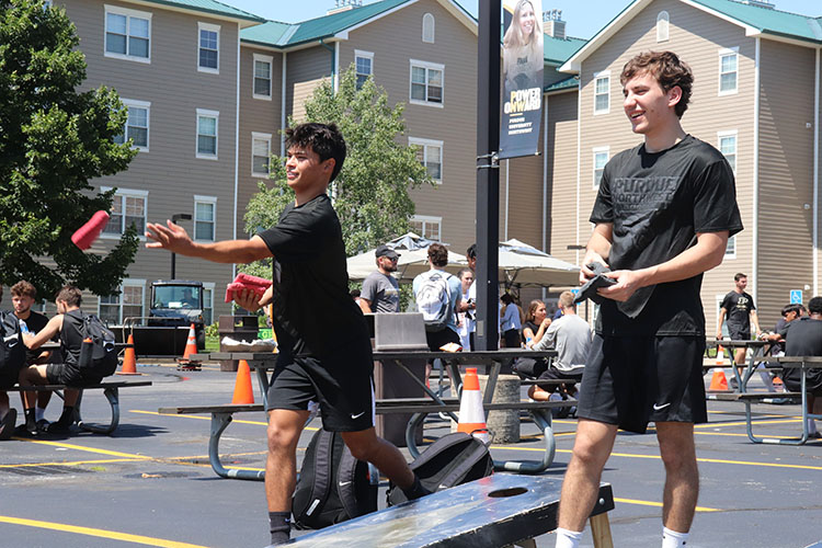 Two people play cornhole in the housing parking lot