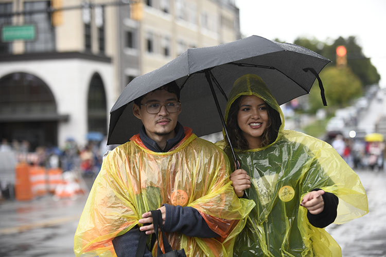 Two students wear yellow ponchos and walk together under an umbrella