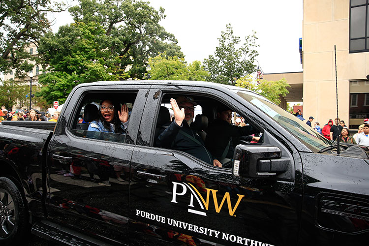 PNW Chancellor Kenneth C. Holford sits in the passenger seat of a black PNW branded truck and waves out the window. There is someone in the seat behind him as well