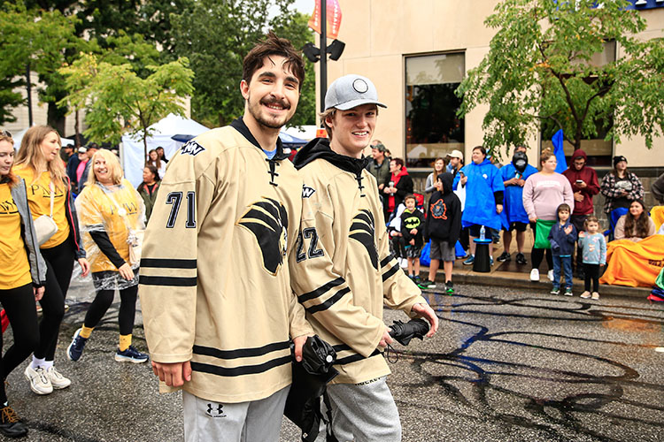 Two members of the PNW hockey team walk down a road. There are people standing on the sidewalks