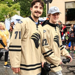 Two members of the PNW hockey team walk down a road. There are people standing on the sidewalks