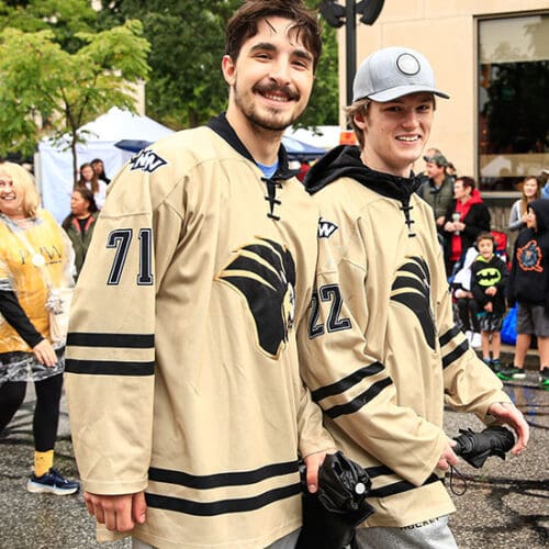 Two members of the PNW hockey team walk down a road. There are people standing on the sidewalks