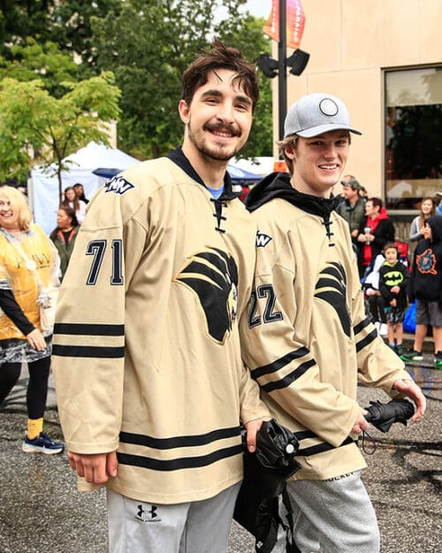 Two members of the PNW hockey team walk down a road. There are people standing on the sidewalks