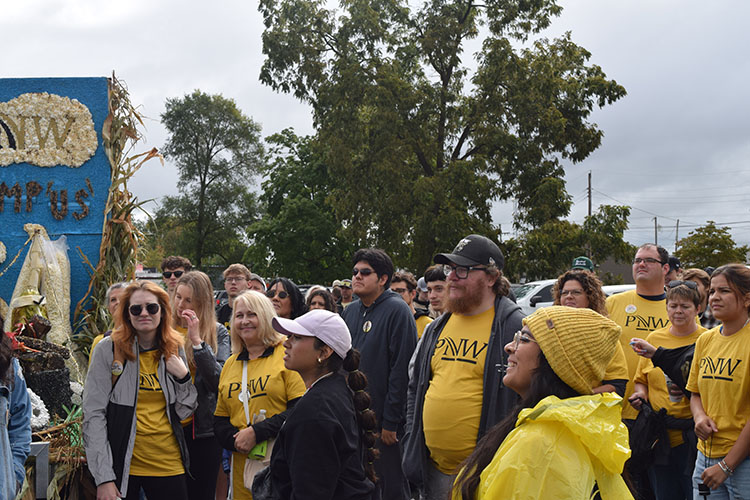 A crowd stands together near the PNW float. Many of them are wearing gold "PNW" t-shirts