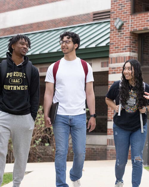 Three students walk down a sidewalk