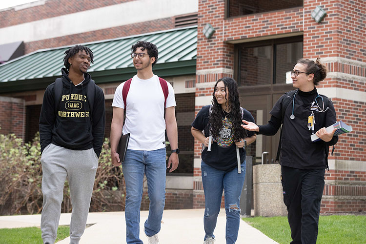 Four students walk down a sidewalk together. There is a brick building in the background