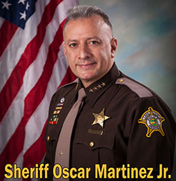 Sheriff Oscar Martinez Jr. in dress uniform in front of an American flag