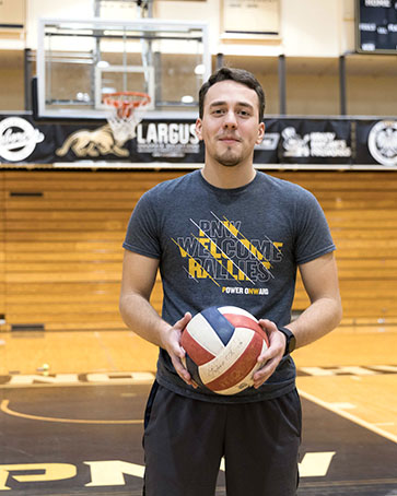 A PNW international student holds a volleyball in a campus gym