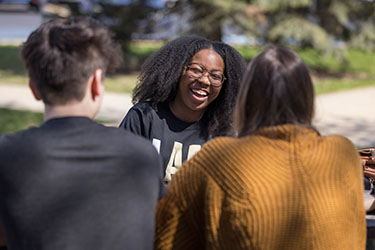 Three students sit at a table. Only one student is facing the camera