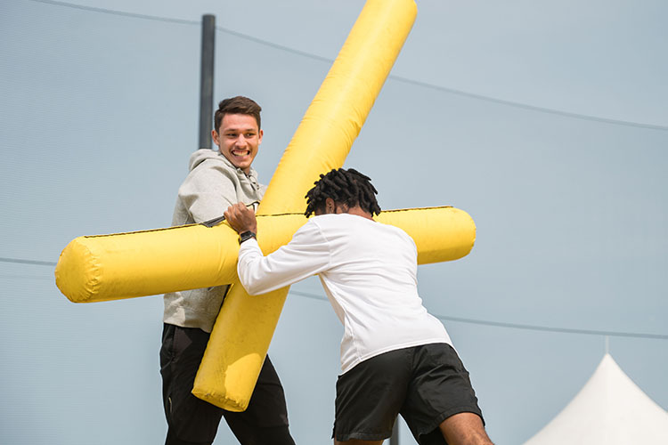 Two students use inflatable sticks to push against each other