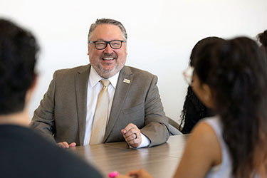 PNW chancellor Chris Holford talks with students at a conference table.