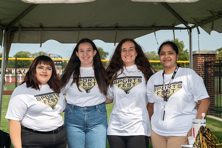 Four students stand together. They are all wearing white "Sports Fest" t-shirts