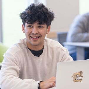 A student sits at a table and works on a laptop