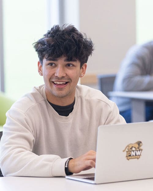 A student sits at a table and works on a laptop