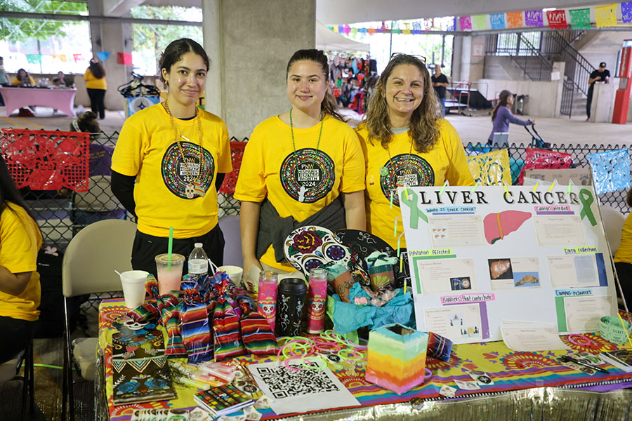 Tres personas con camisetas amarillas del Mes de la Herencia Hispana posan juntas detrás de una mesa