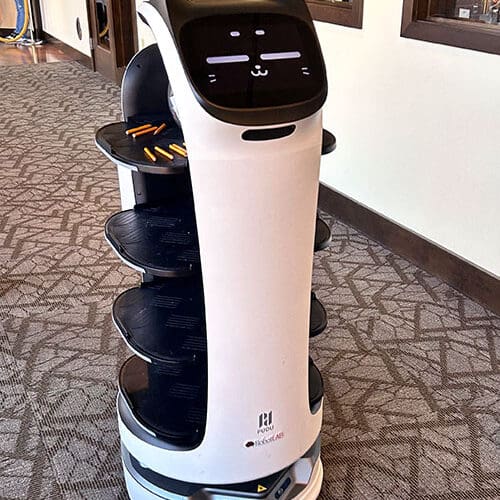 A cylindrical robot carries snacks in a hallway