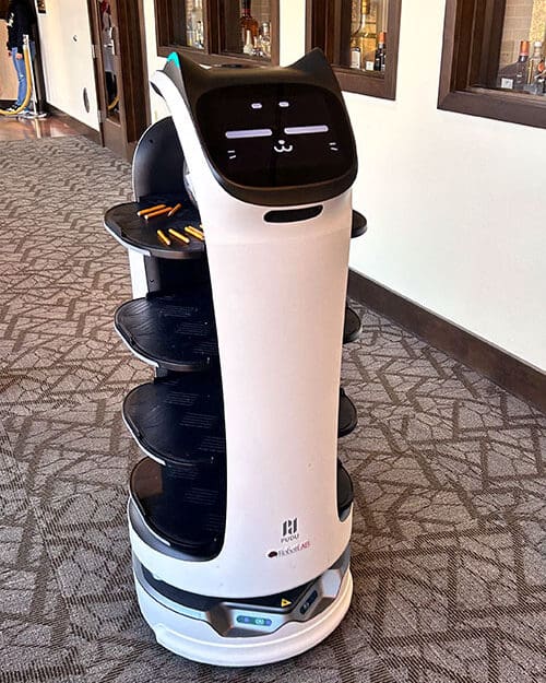 A cylindrical robot carries snacks in a hallway