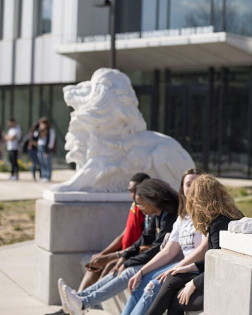 PNW students sit by a lion sculpture in front of the Nils K. Nelson Bioscience Innovation Building