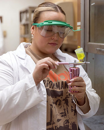 A PNW student in a lab coat and goggles works in a lab