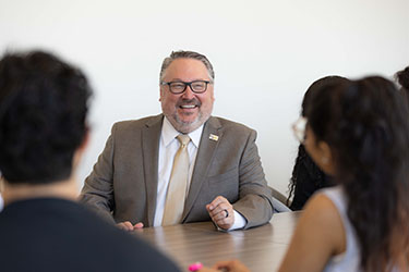 PNW chancellor Chris Holford talks with students at a conference table.