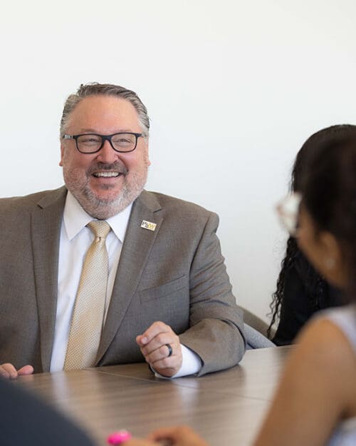 PNW chancellor Chris Holford talks with students at a conference table.