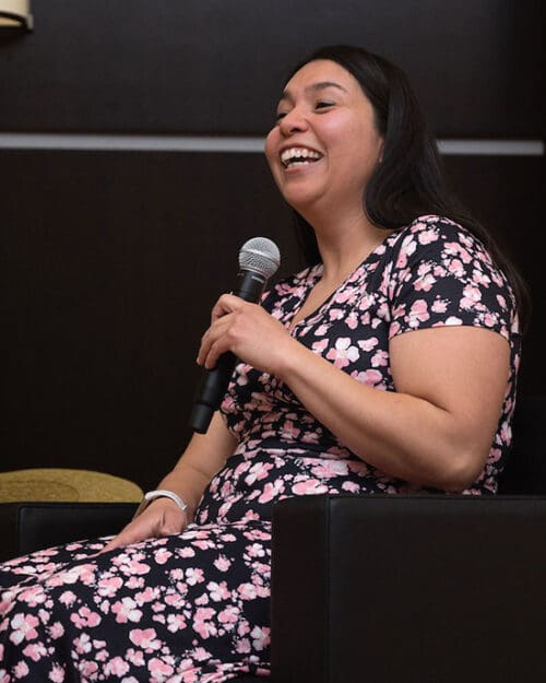 Sandra Patino (MA’19) sits on stage holding a microphone.