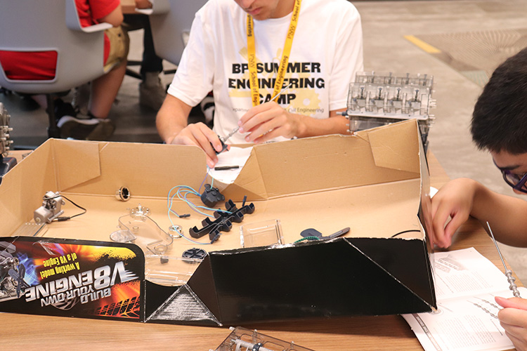 Two engineering camp participants working on building a V8 engine.