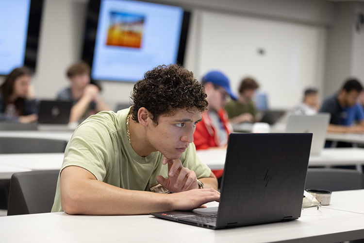 A student in a green shirt works on a laptop